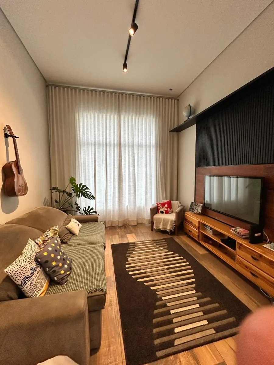 Sala residencial acolhedora em Itatiba com cortina dupla cinza e violão na parede, ambiente vivo e curadoria de tecidos da Neusa