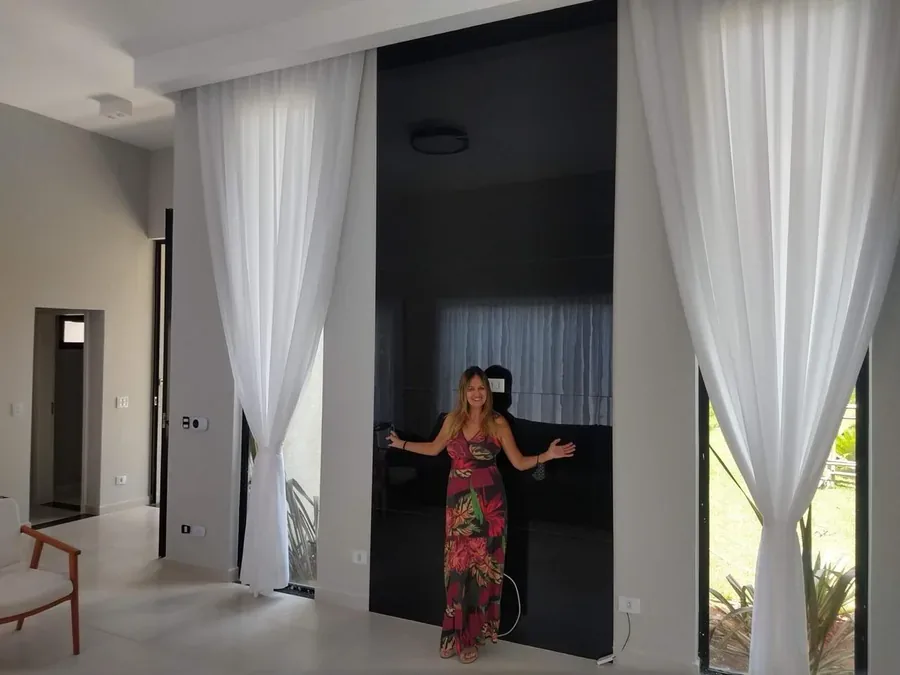 Neusa Quintanilia em frente a cortinas brancas sob medida em ambiente residencial de pé direito alto